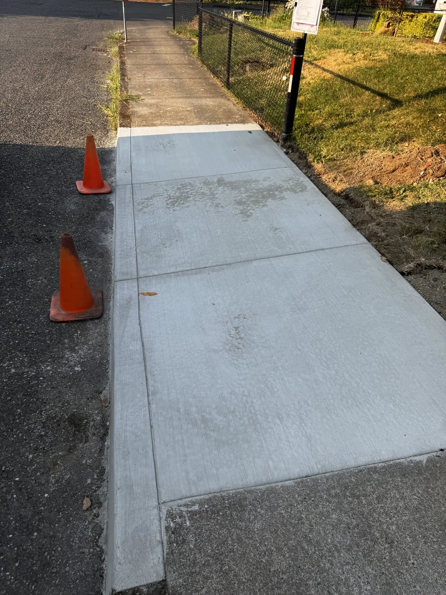 New concrete sidewalk along a street, coned off while it cures