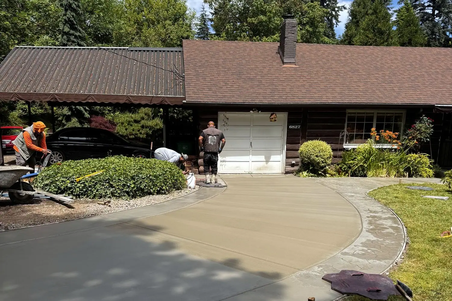 MJ Concrete crew finishing a curved concrete driveway in front of a home