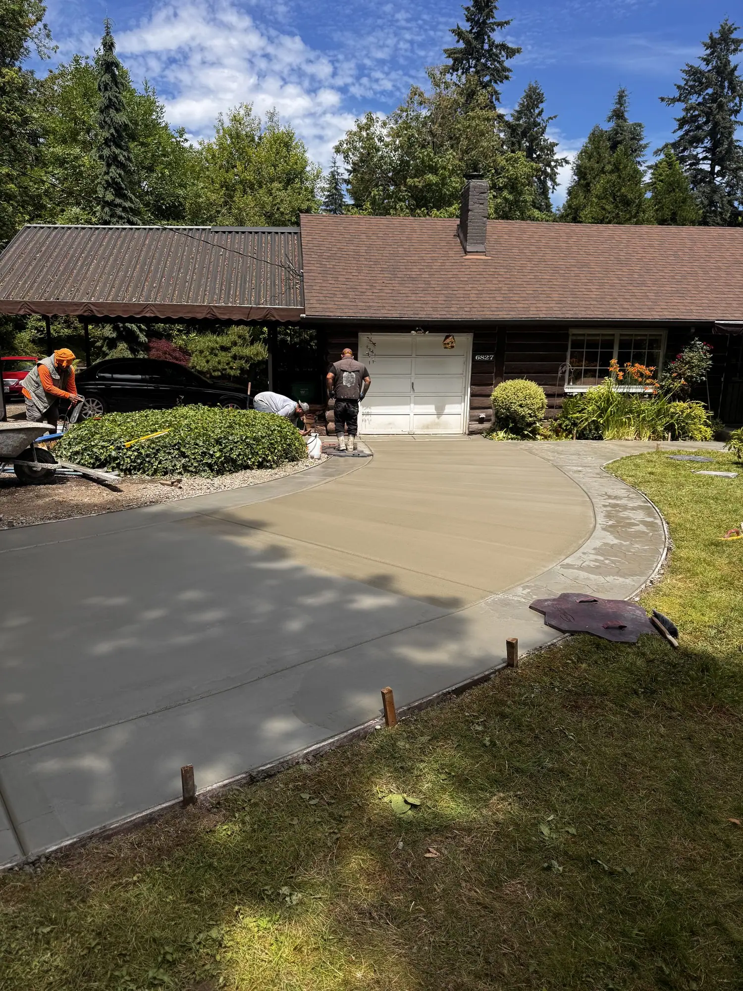 MJ Concrete crew finishing a curved concrete driveway in front of a home
