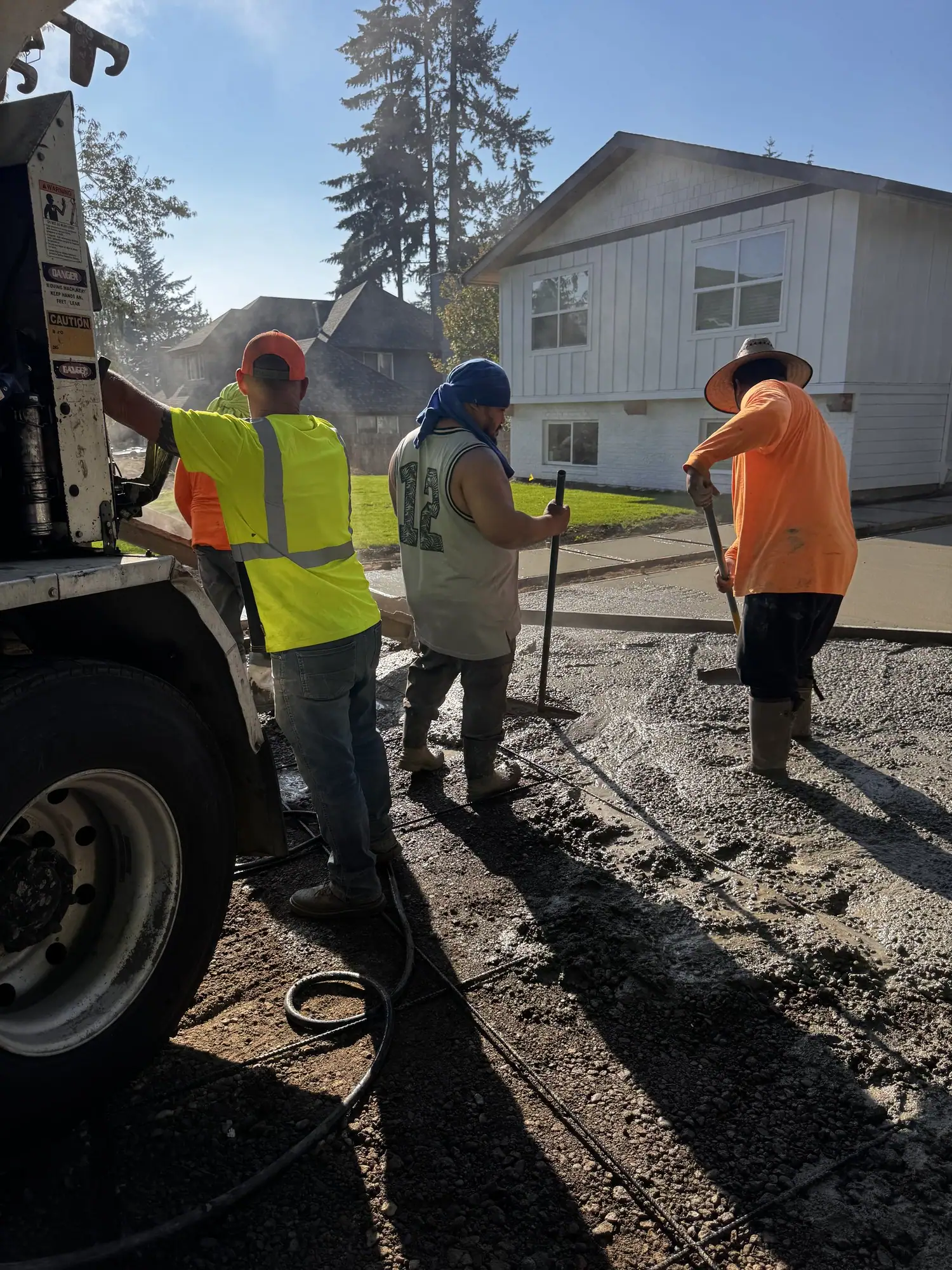 Concrete truck pouring a driveway while the MJ Concrete crew spreads it