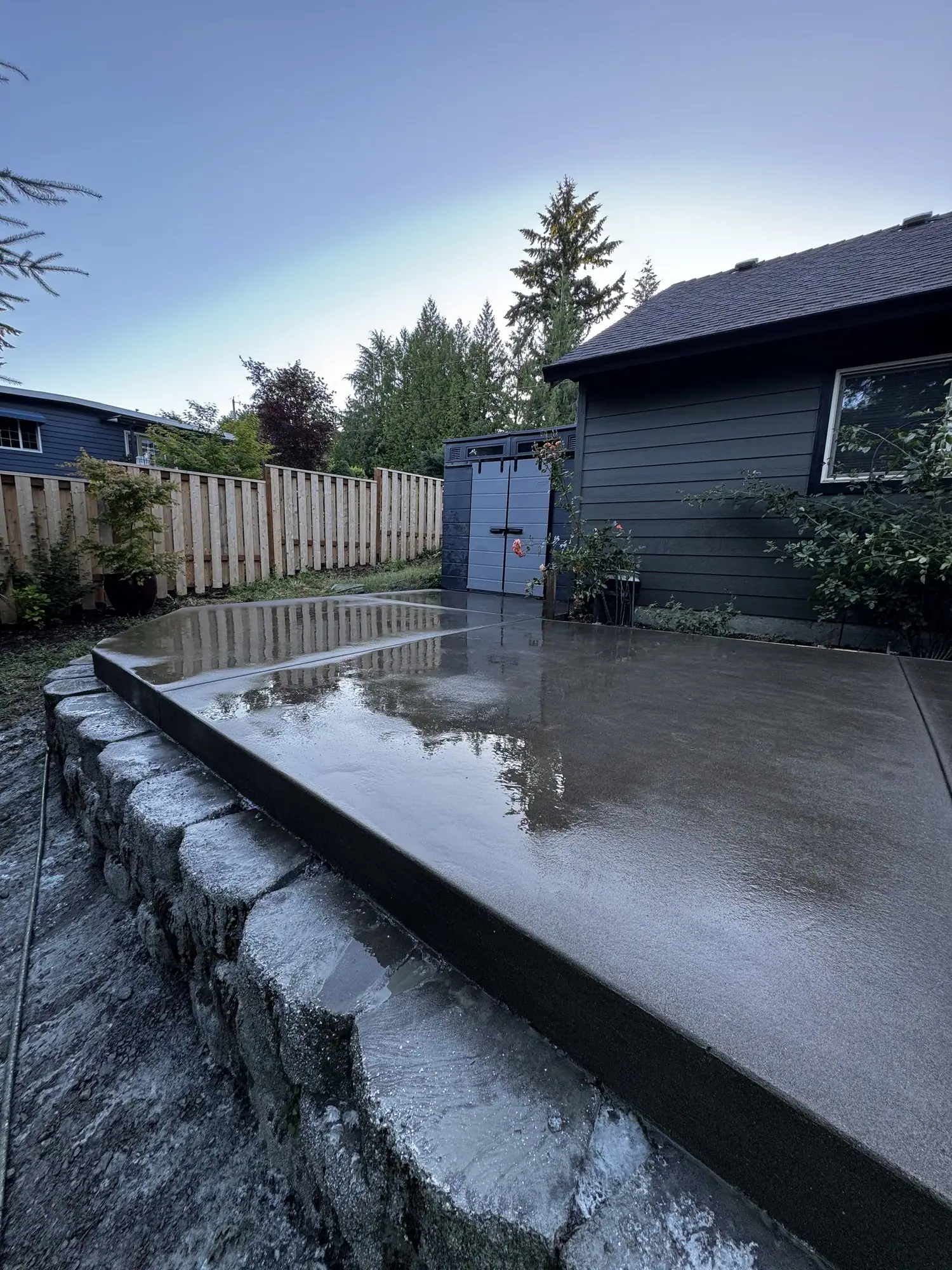 Concrete patio slab with a poured concrete edge wall above a rock wall