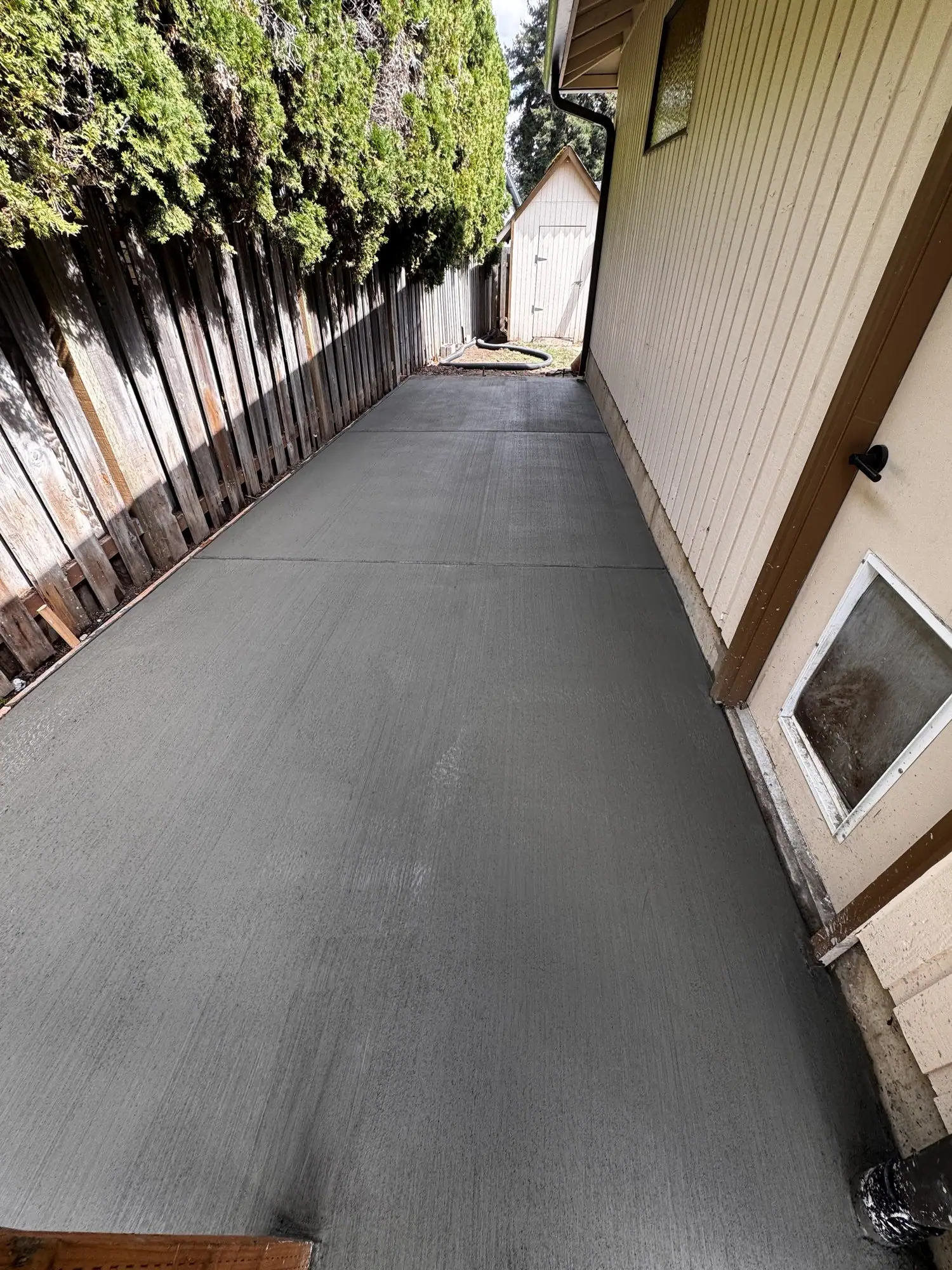 Concrete slab poured along a narrow side yard between a fence and a house