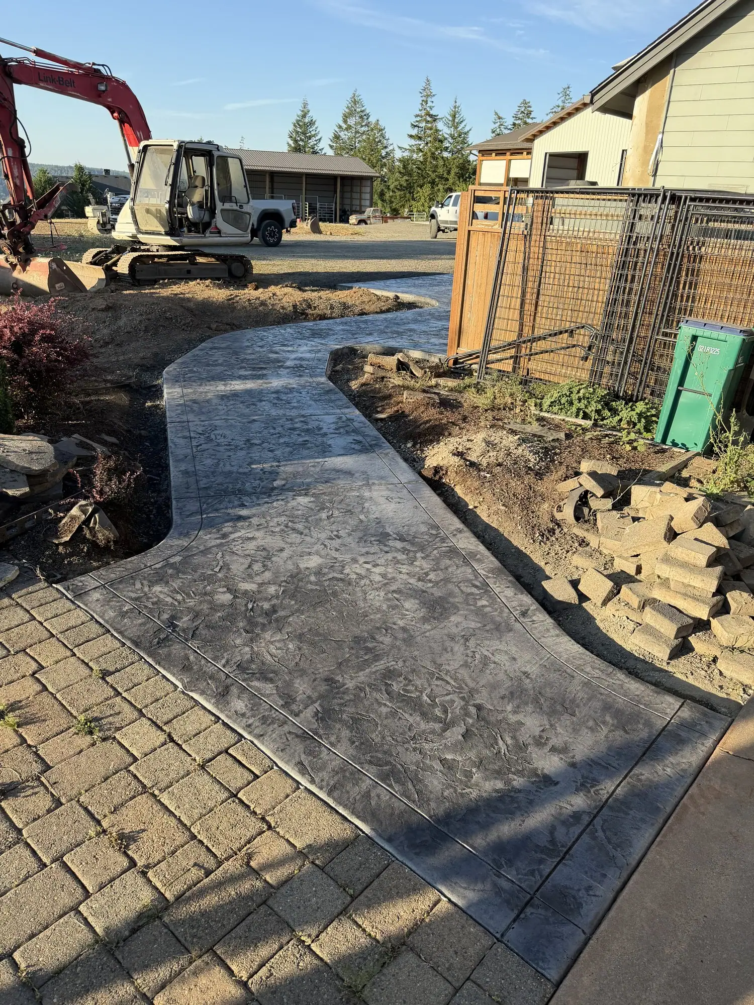 Curved gray stamped concrete path through a landscaped yard