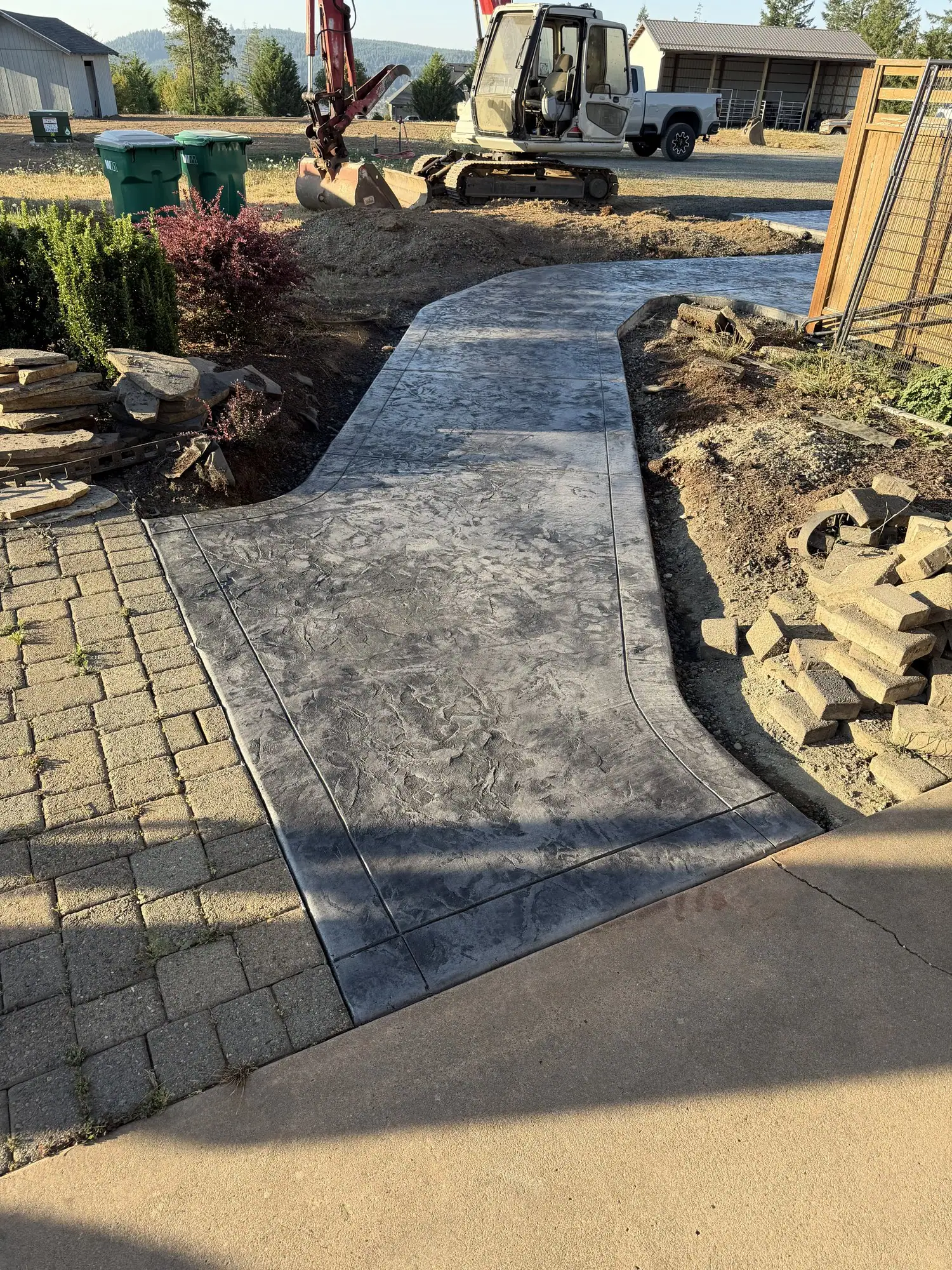 Curved stamped concrete walkway next to a paver patio